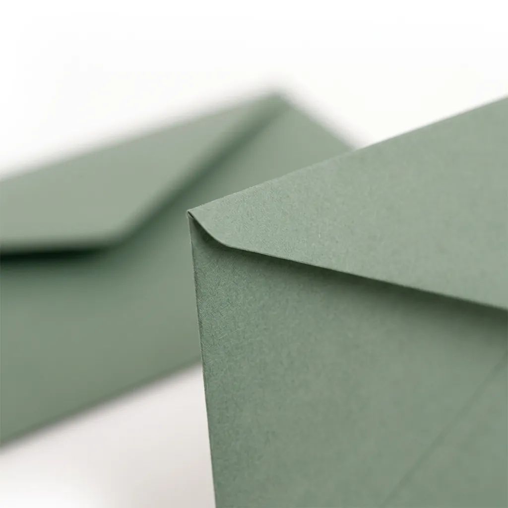 Dwie koperty ozdobne DL w kolorze Matcha — zbliżenie na klapkę i krawędź papieru